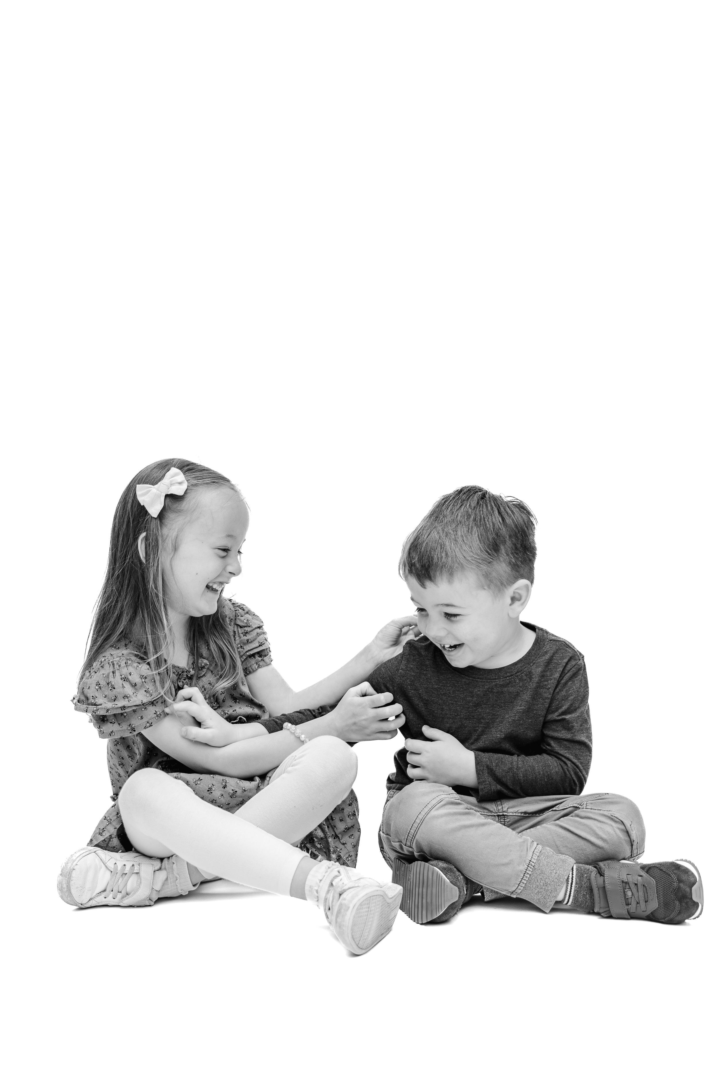 Two young children laugh and play together while sitting on a white background in black and white photo.