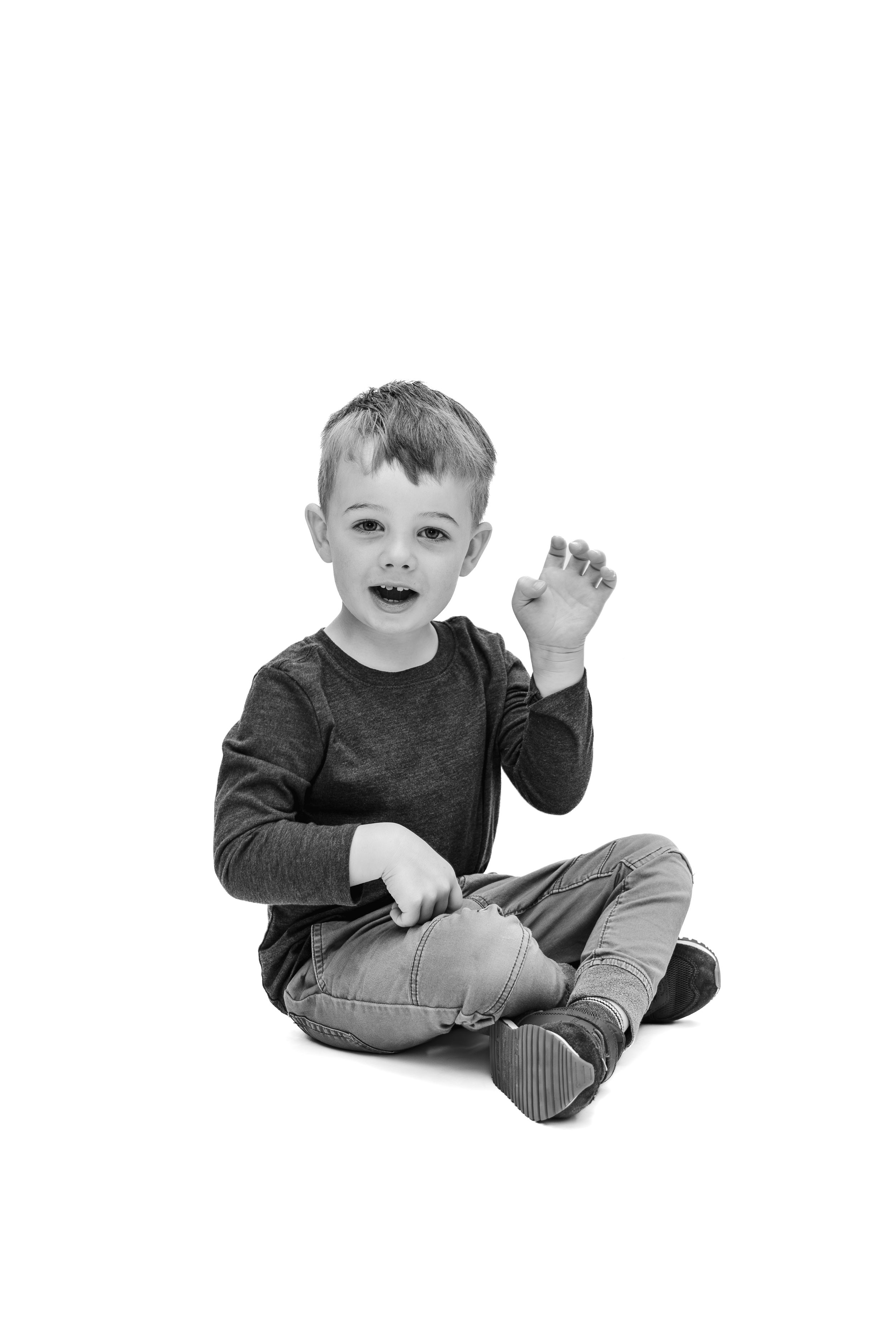 Black and white photo of a young boy sitting cross-legged, smiling and raising his fist on a white background.