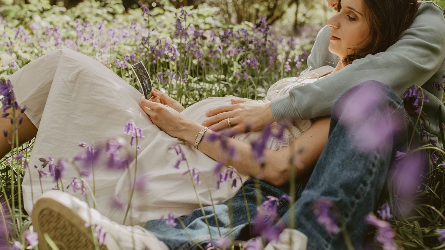 Woman relaxing among purple wildflowers and bluebells in a lush green meadow on a sunny day.
