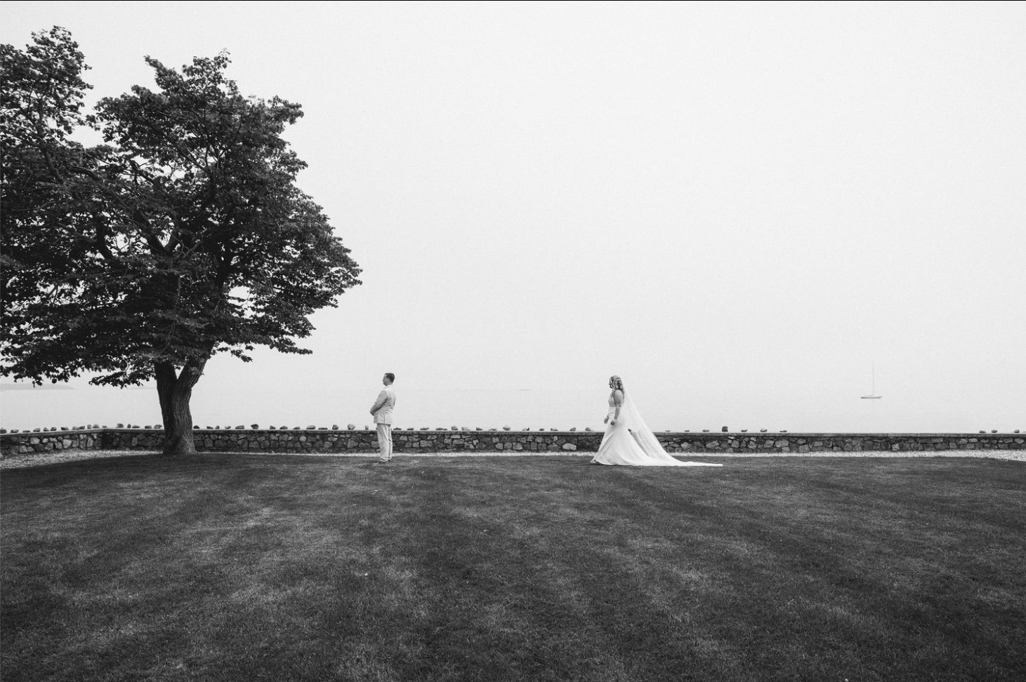 Wedding ceremony setup with white chairs on a lush green lawn facing a historic stone church under cloudy skies.