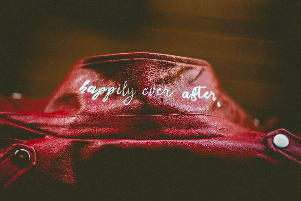 Red leather jacket collar with 'happily ever after' embroidered in white cursive script, close-up detail shot.