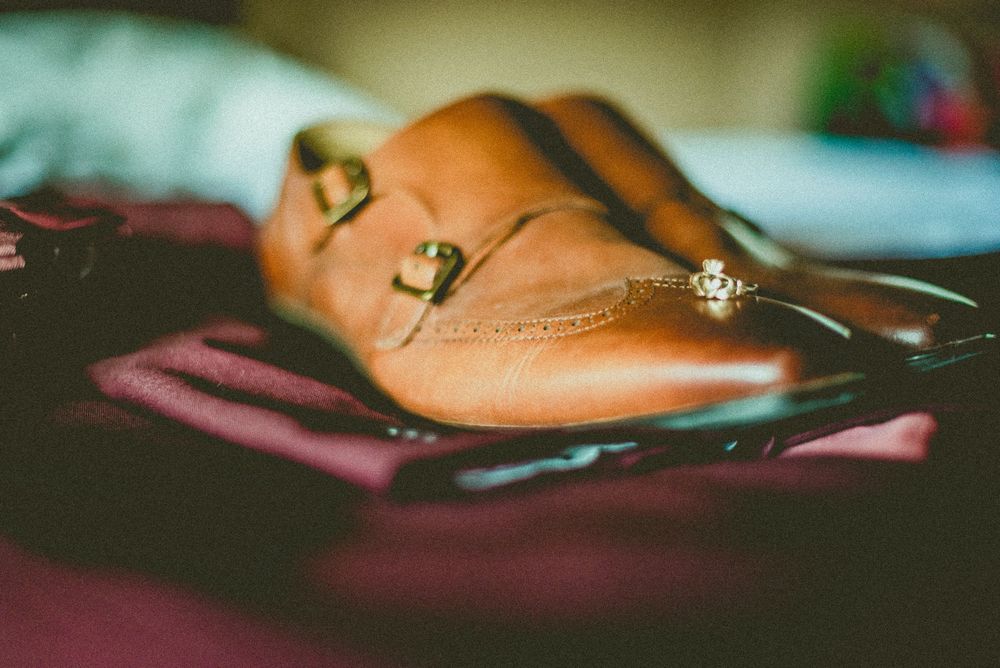 Close-up of tan leather double monk strap dress shoes with gold buckles on a burgundy surface.
