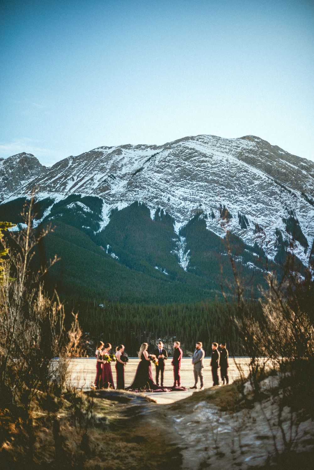 Wedding ceremony group standing before a snow-capped mountain backdrop under a clear blue sky.
