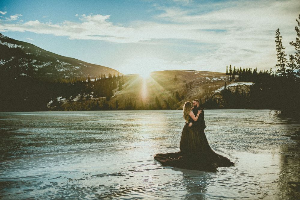 Couple embracing in a mountain lake at sunset with golden light reflecting on the water.