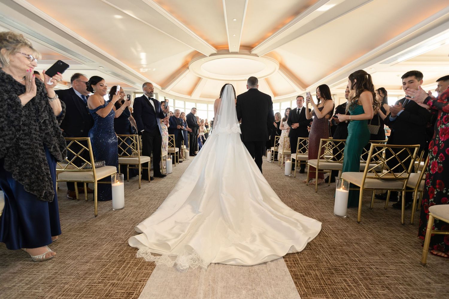 Bride wearing a long cathedral veil walking down the aisle toward her wedding ceremony in Westchester County, New York.