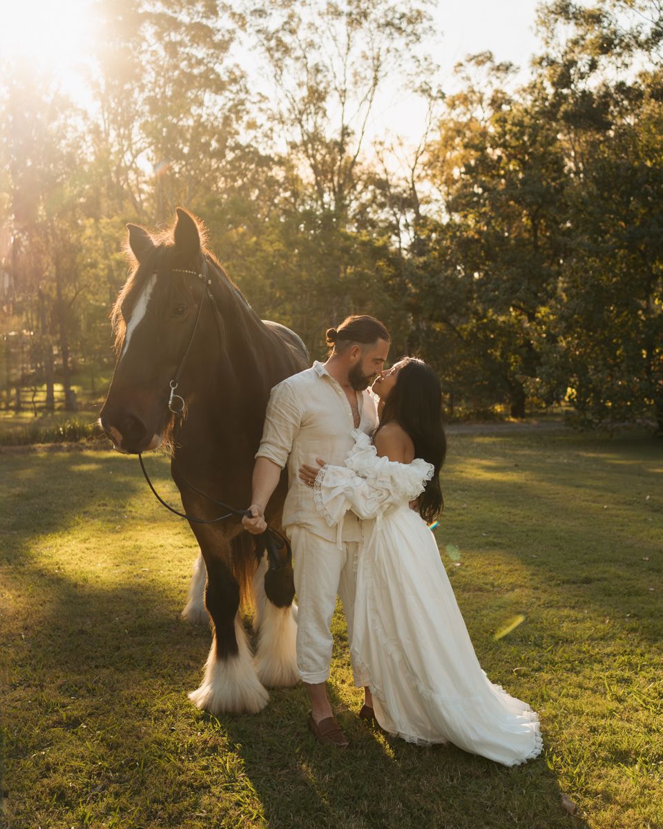 Couple sharing a romantic kiss in wedding attire beside a horse at golden hour in a lush garden photoshoot in sydney photoshoot with horse