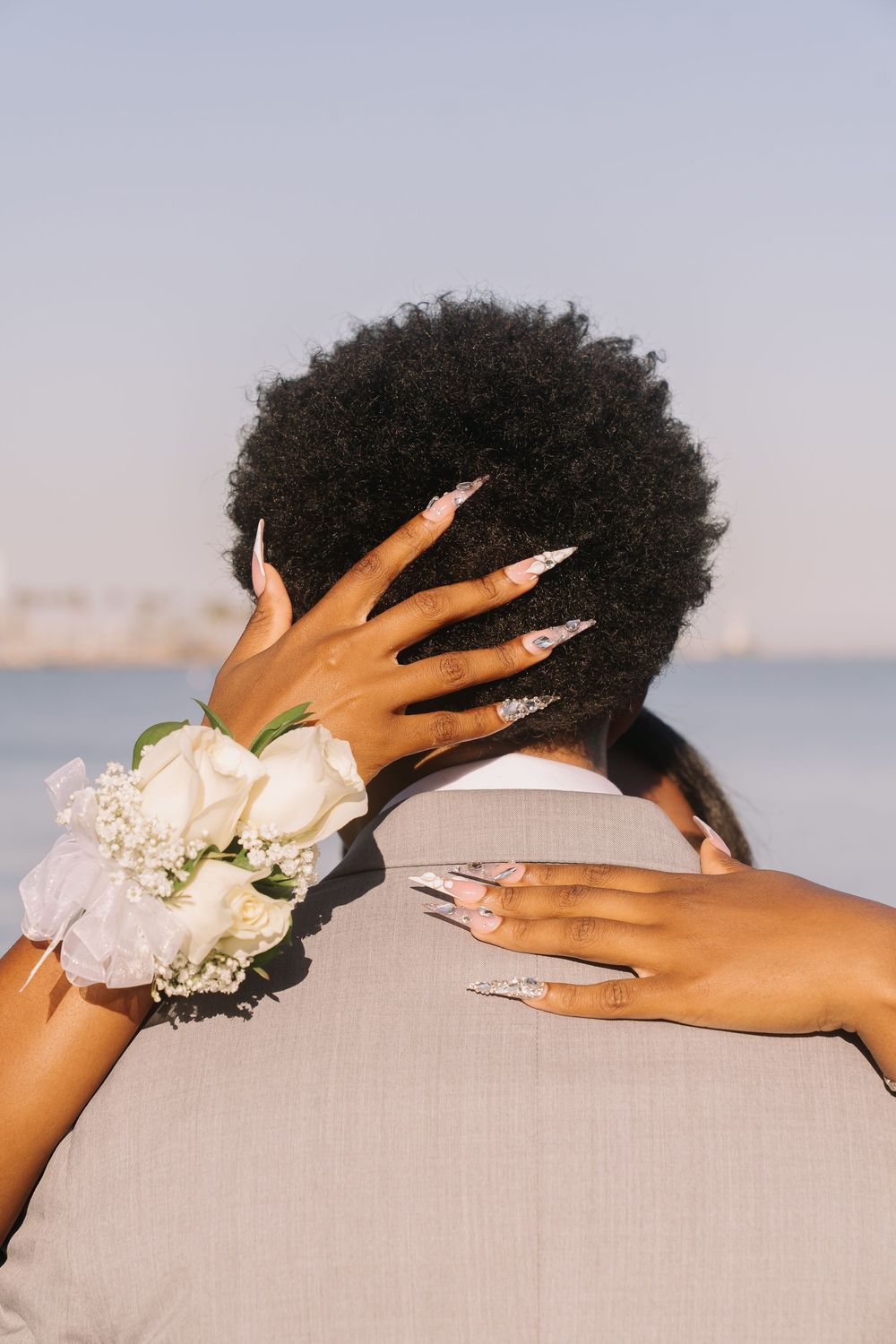 Close-up of a prom couple embracing, showcasing a white rose wrist corsage and elegant stiletto nails.