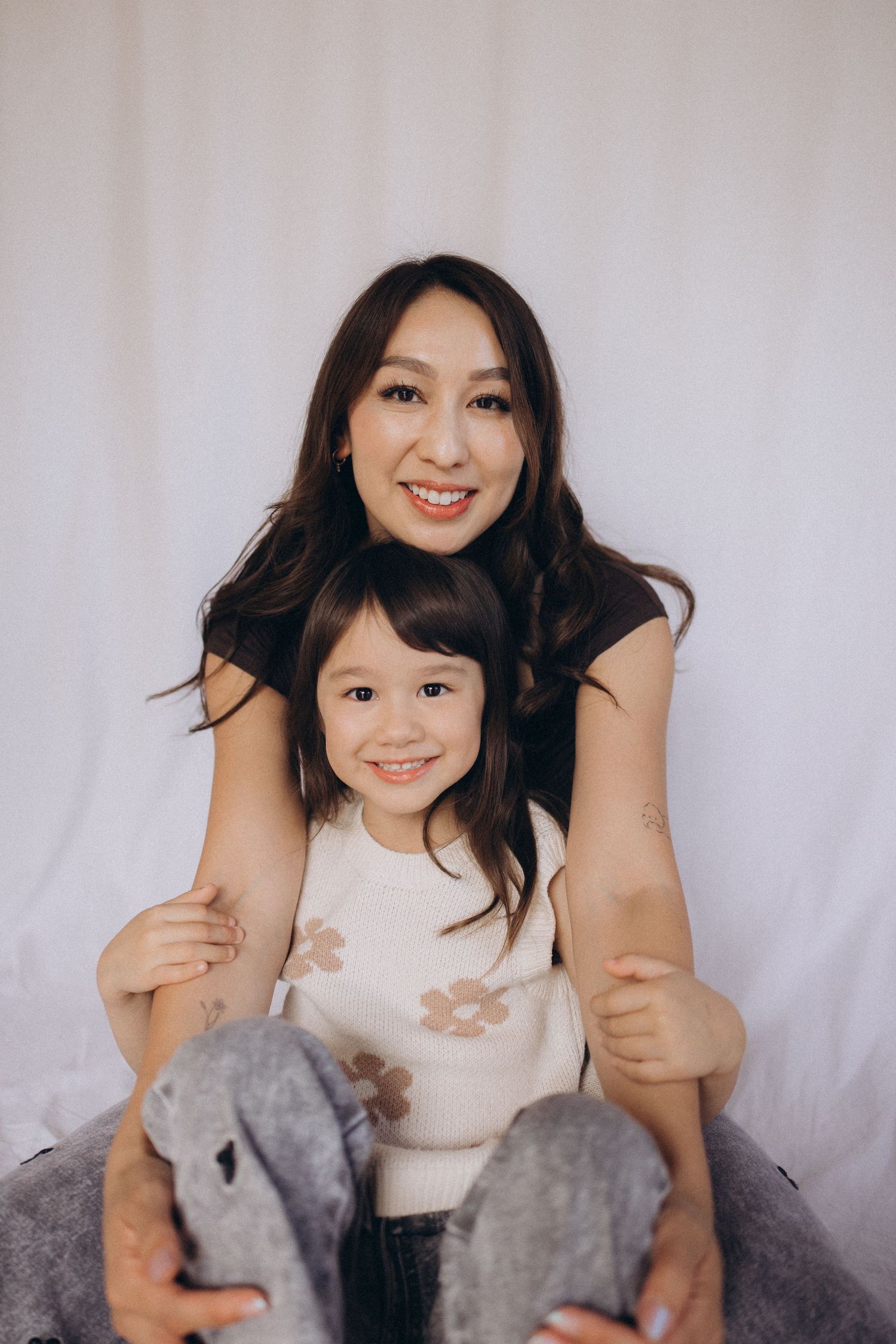 A smiling mother and young daughter pose together against a white fabric backdrop in a portrait photo studio in New Zealand..