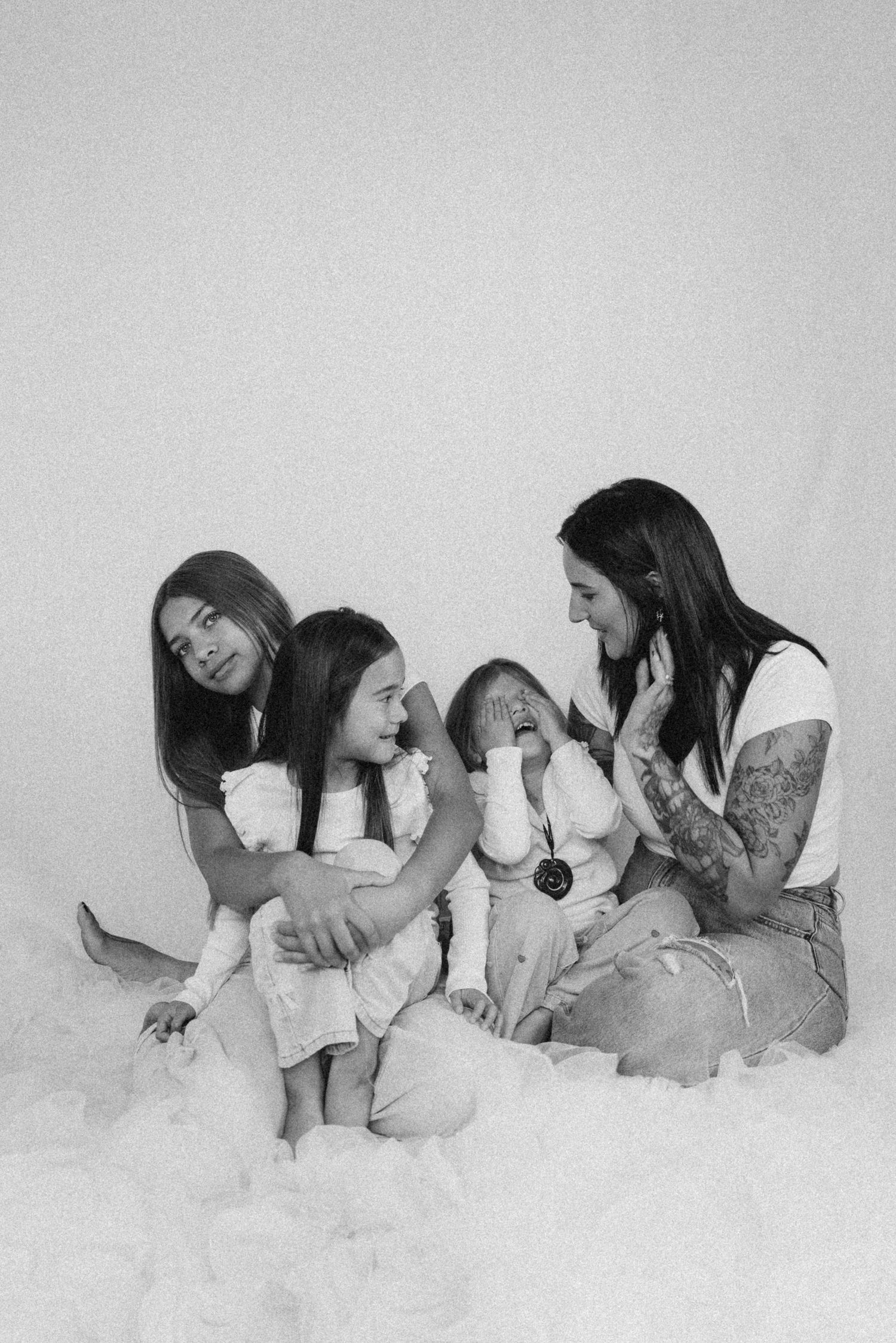 Black and white photo of a tattooed mother laughing with her three daughters on a white backdrop in New Zealand..