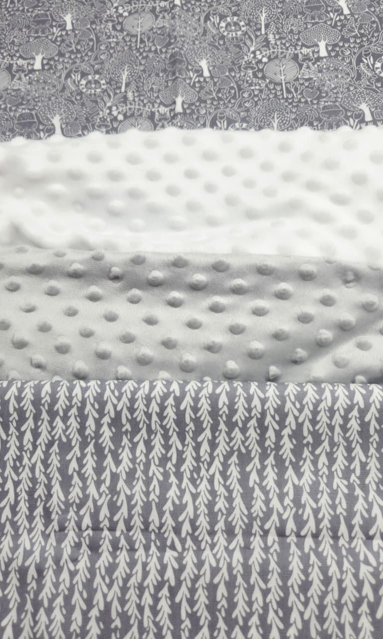 Gray and white fabric swatches featuring forest animals print, soft minky dot texture, and delicate pine tree pattern.