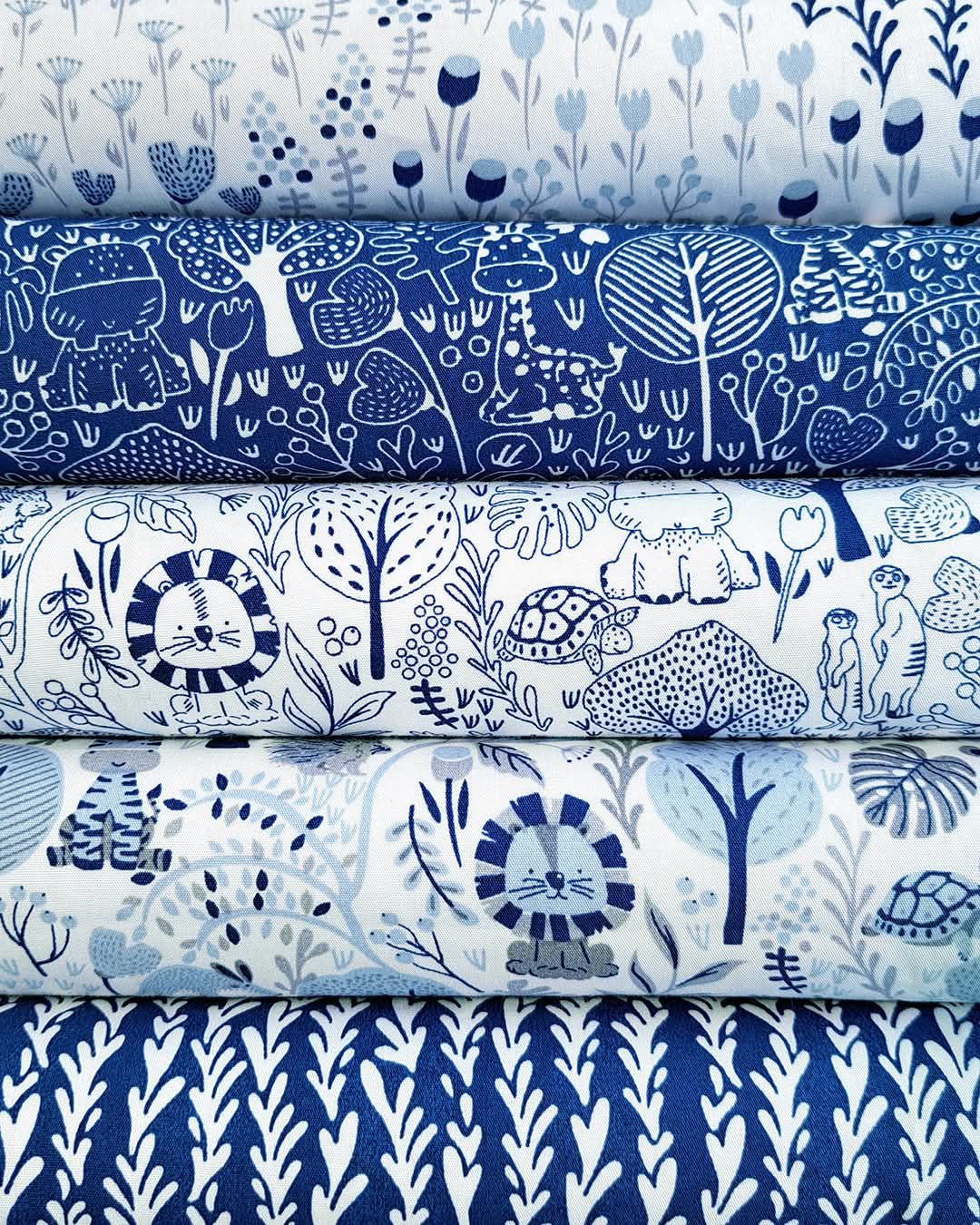 Stack of blue and white fabric bolts featuring whimsical animal and nature prints in various indigo patterns.
