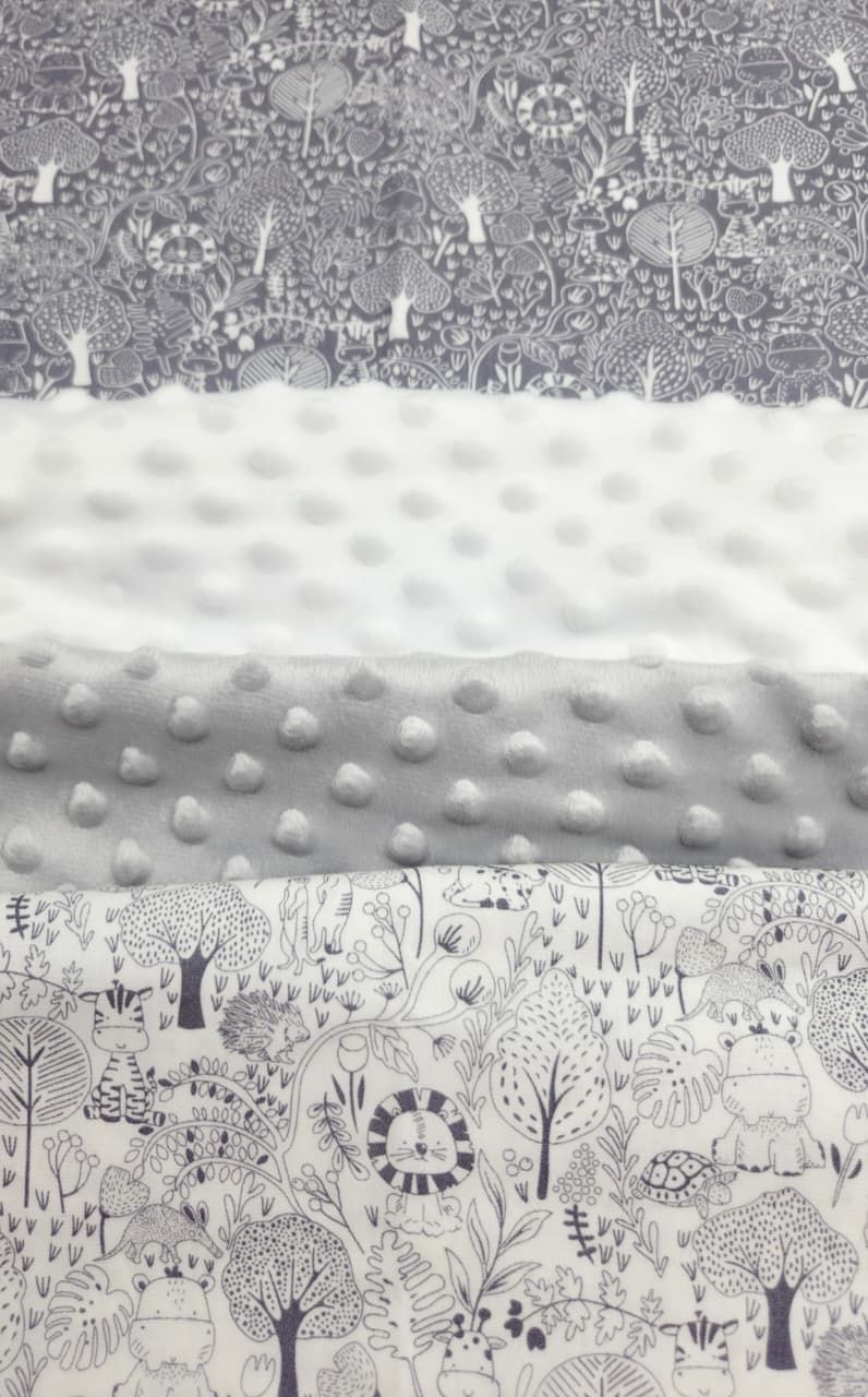 Gray and white minky dot fabric alongside woodland animal print cotton fabric swatches for baby quilts.