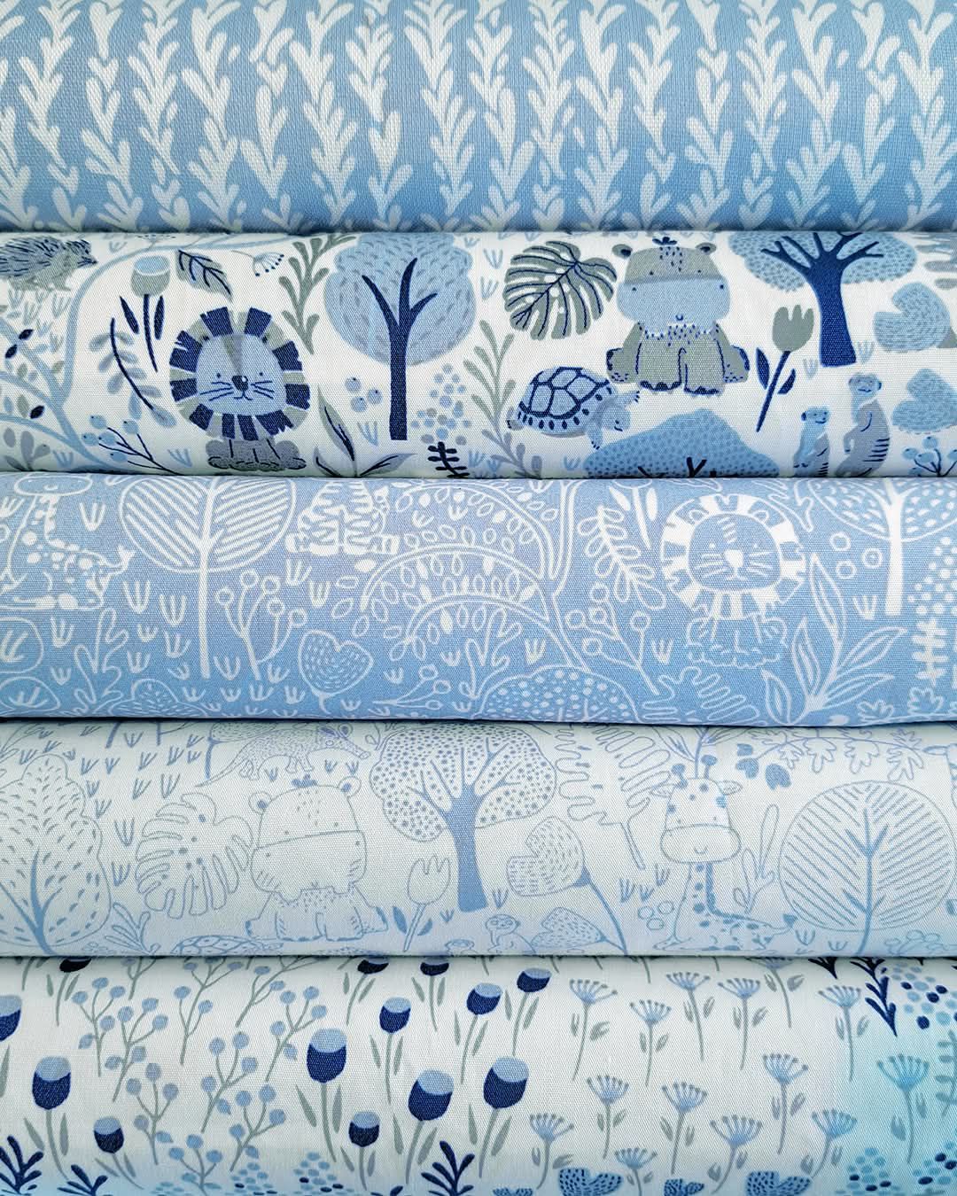 Stack of blue and white fabric rolls featuring whimsical jungle animals, lions, turtles, and botanical prints for quilting.