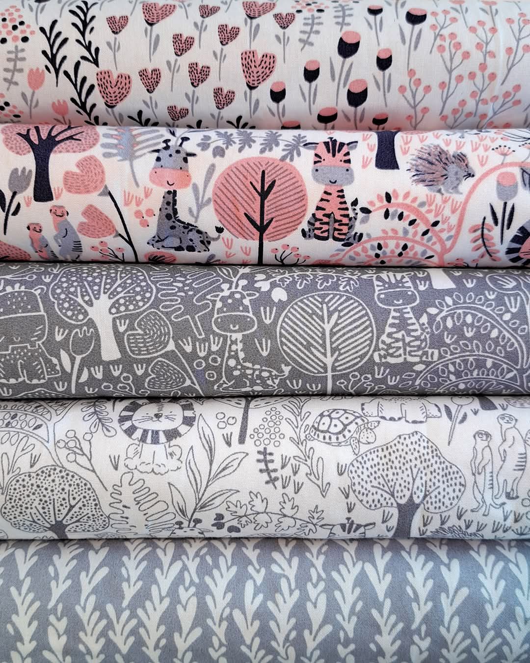 Stack of five rolled fabric bolts featuring whimsical woodland animal prints in pink, gray, and white colorways.