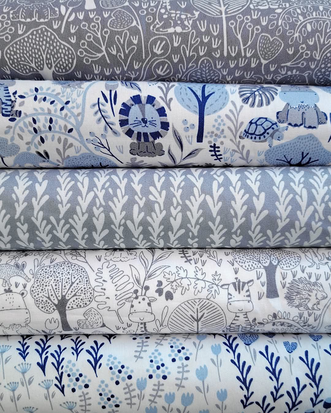 Stack of blue and gray animal print fabric rolls featuring lions, turtles, and forest scenes in a charming children's textile design.