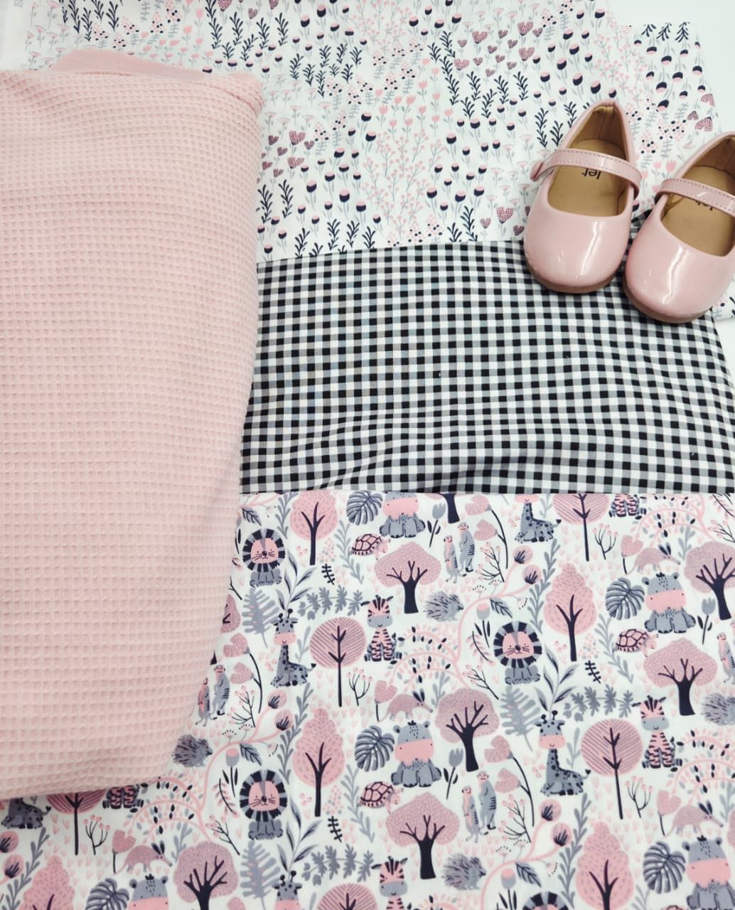 Pink waffle knit fabric, gingham check cloth, floral print fabric, and pink Mary Jane shoes arranged in a flat lay display.