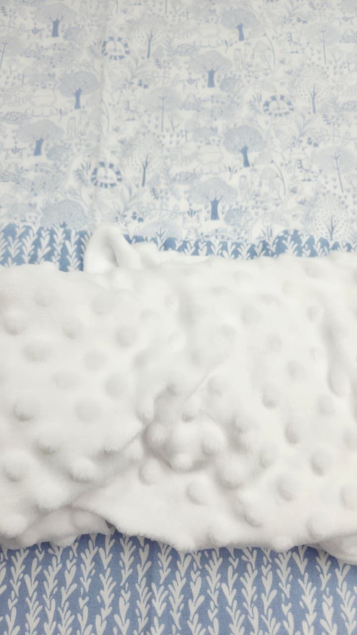 Soft white minky dot baby blanket with blue and white woodland forest print fabric backing.