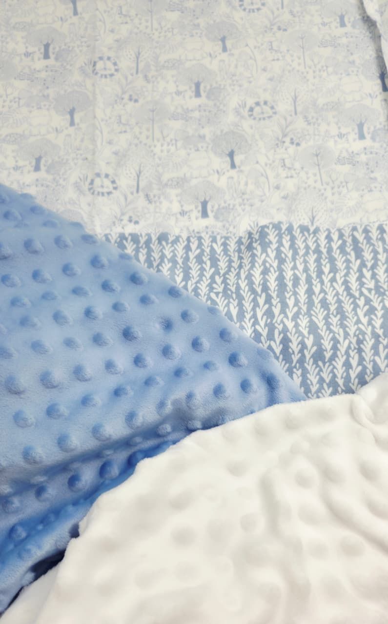 Blue minky dot and white patterned baby blanket fabrics with forest and leaf prints layered together.