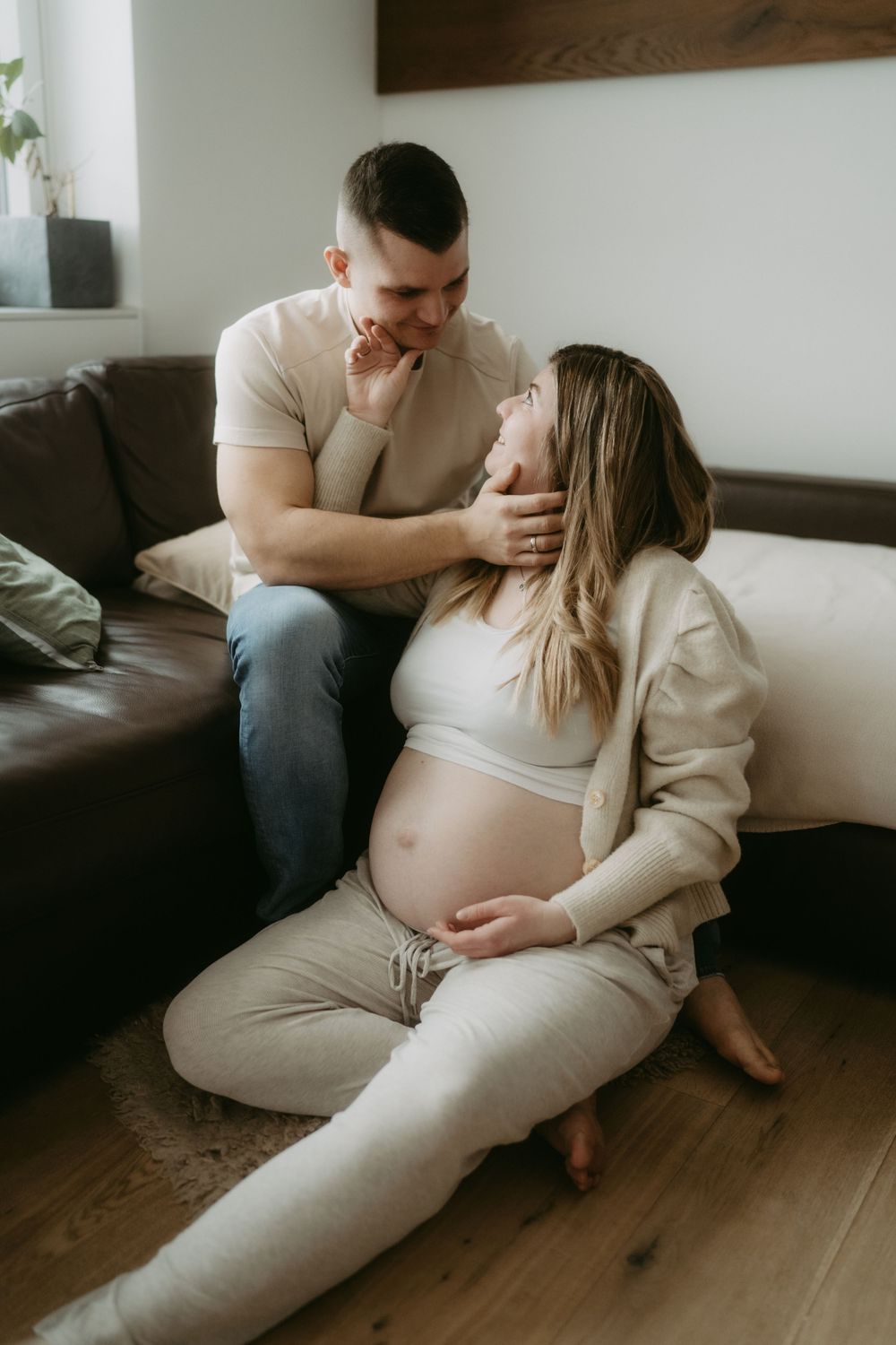 Pregnant woman sitting on floor leaning against sofa while partner gently touches her face.