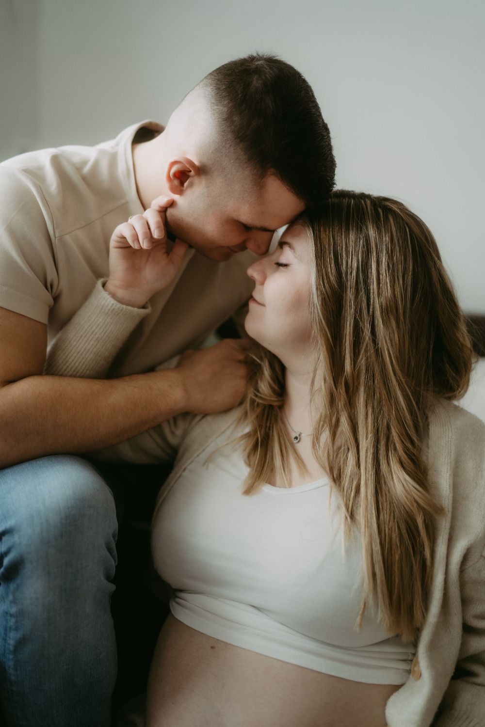 Couple sharing a tender moment, pregnant woman with baby bump leaning close as partner kisses her forehead.