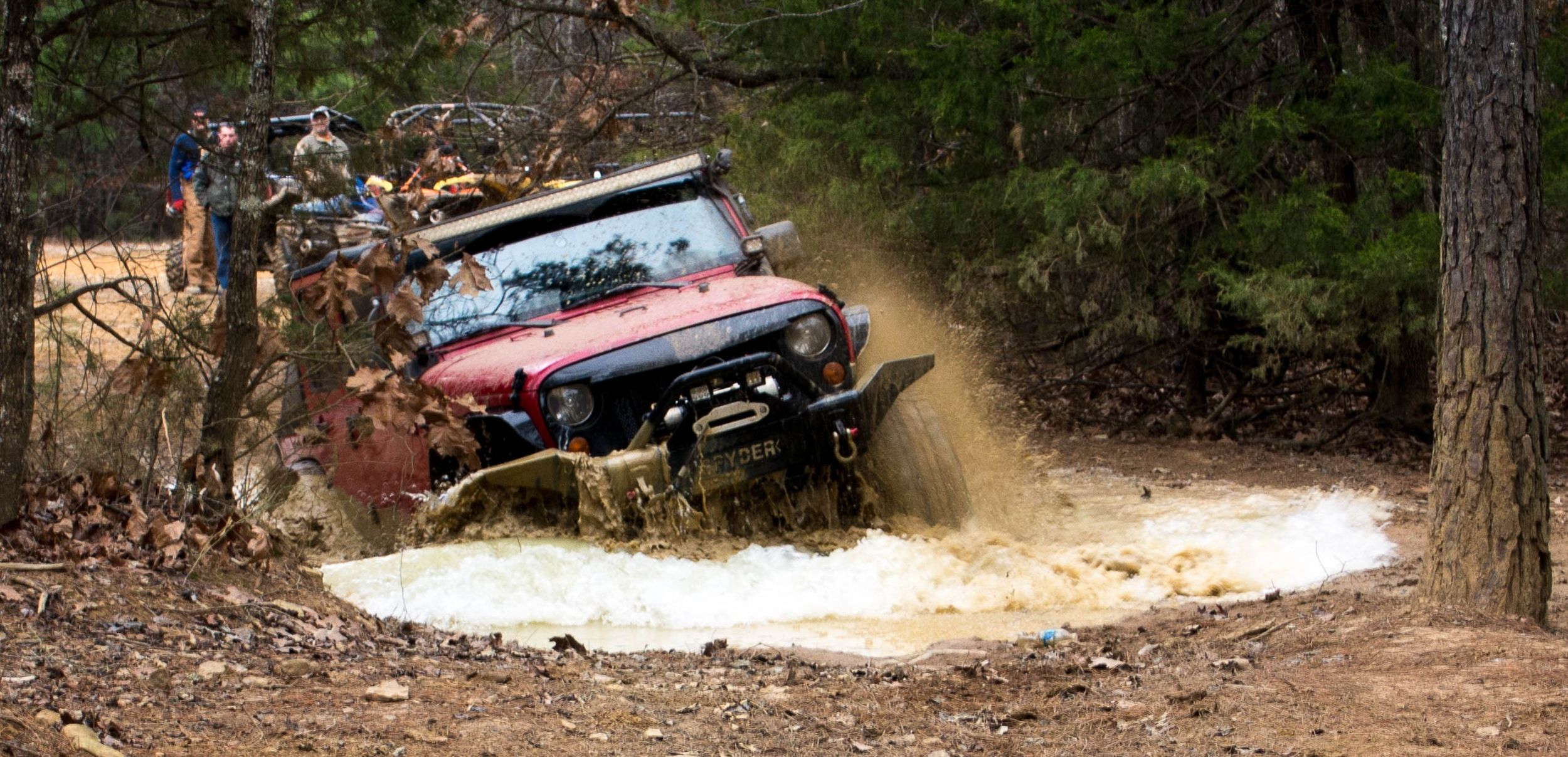 Red Jeep Wrangler off-road through mud pit at outdoor event Northwest Arkansas