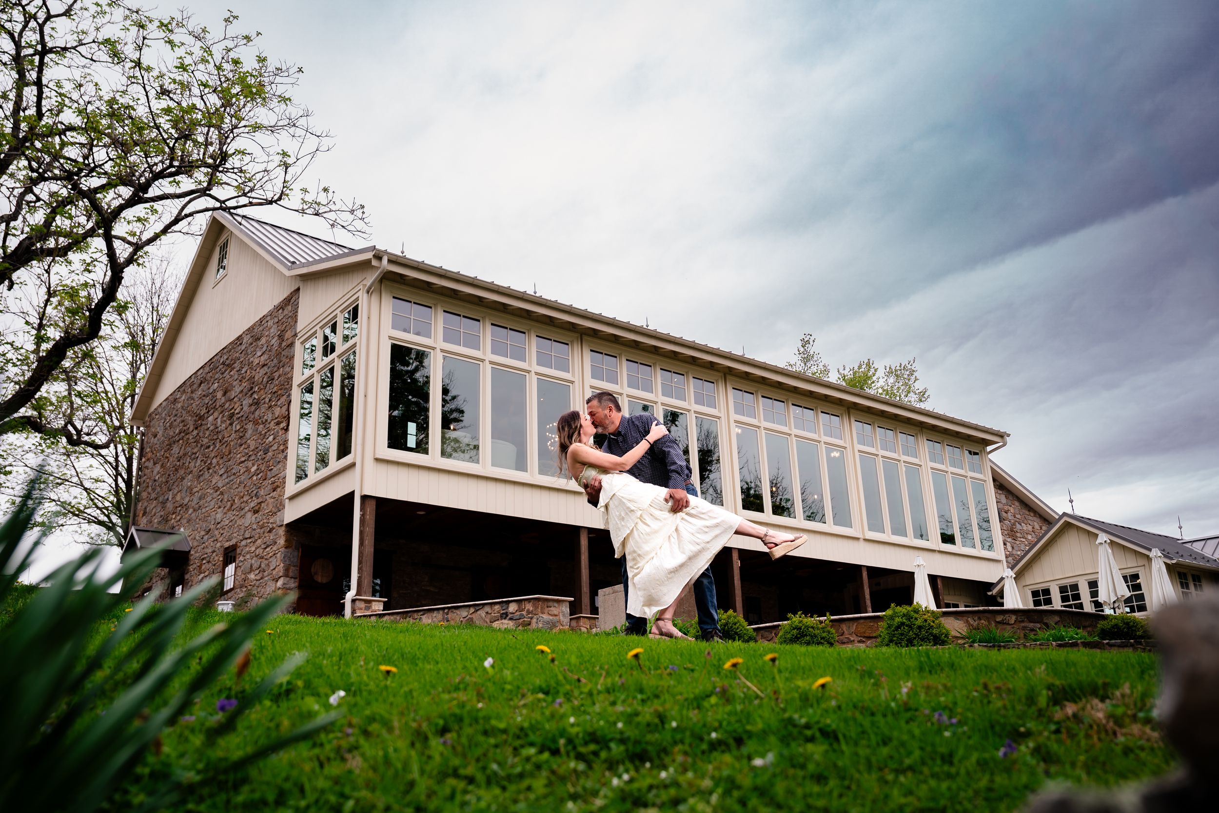 Groom dipping bride dramatically in front of elegant wedding venue with large windows.