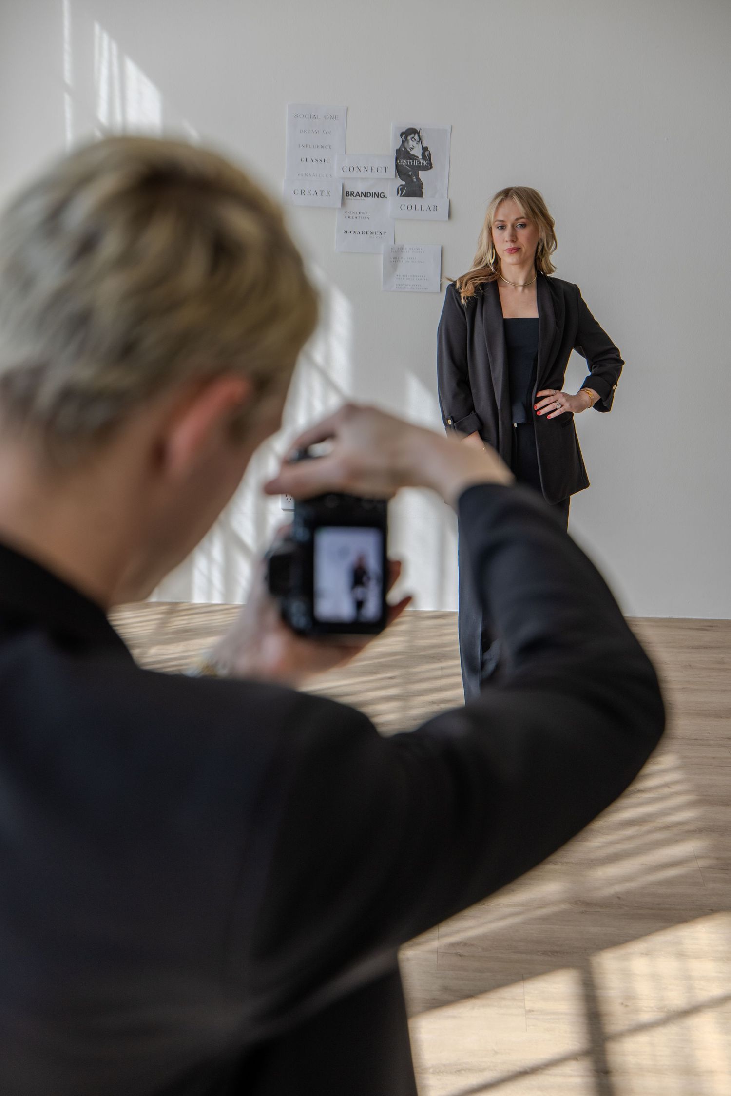 Photographer capturing a blonde woman posing in a black blazer during a professional photo shoot in a bright studio.