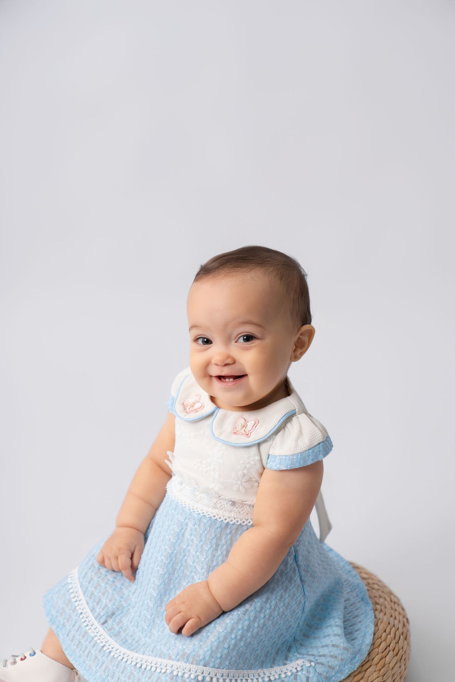 Smiling baby in beige onesie and hat stands behind white wooden ONE blocks for first birthday photo.