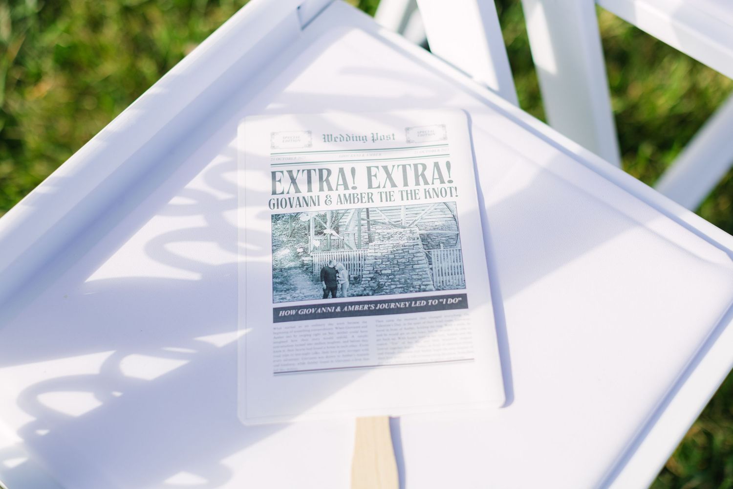 Wedding program designed as a newspaper with 'Extra! Extra!' headline resting on a white chair at an outdoor ceremony.