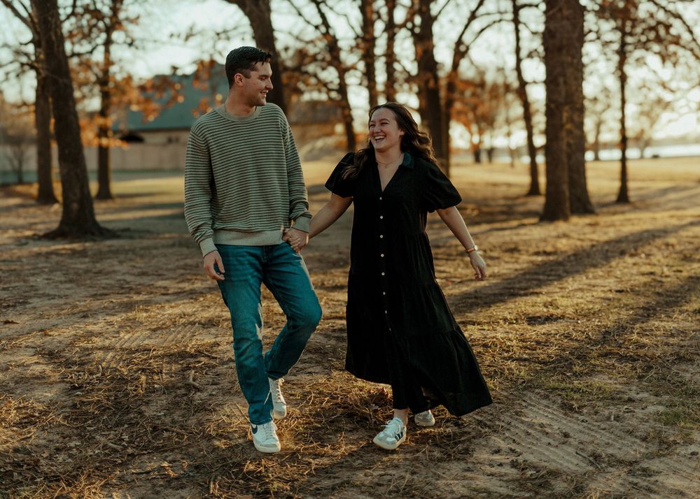 A happy couple walks hand-in-hand through a sunlit autumn park.