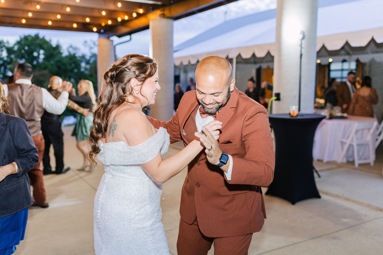 Bride and groom share first dance at outdoor wedding reception under string lights.