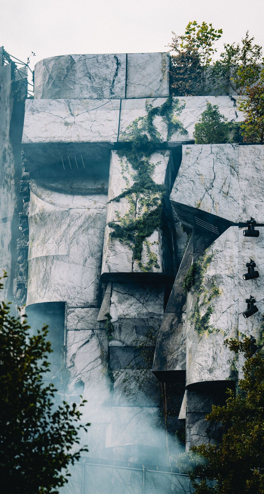 Abstract architectural stage facade with marble-textured panels, climbing vines, and atmospheric fog effects.