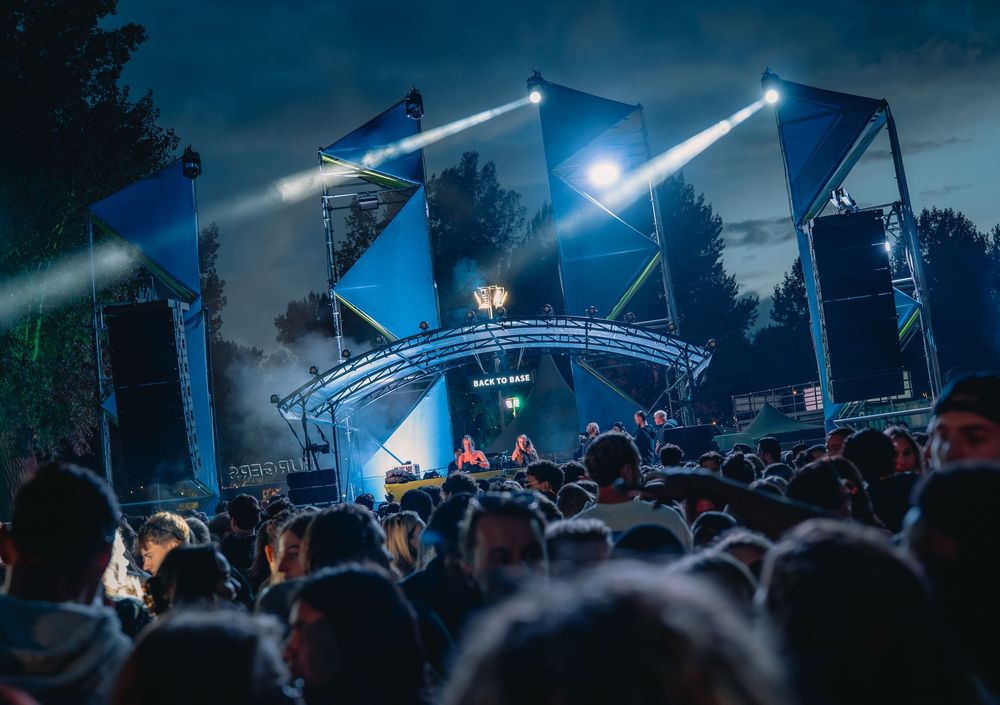 Outdoor festival stage with blue spotlights and a crowd of attendees at a nighttime music event.