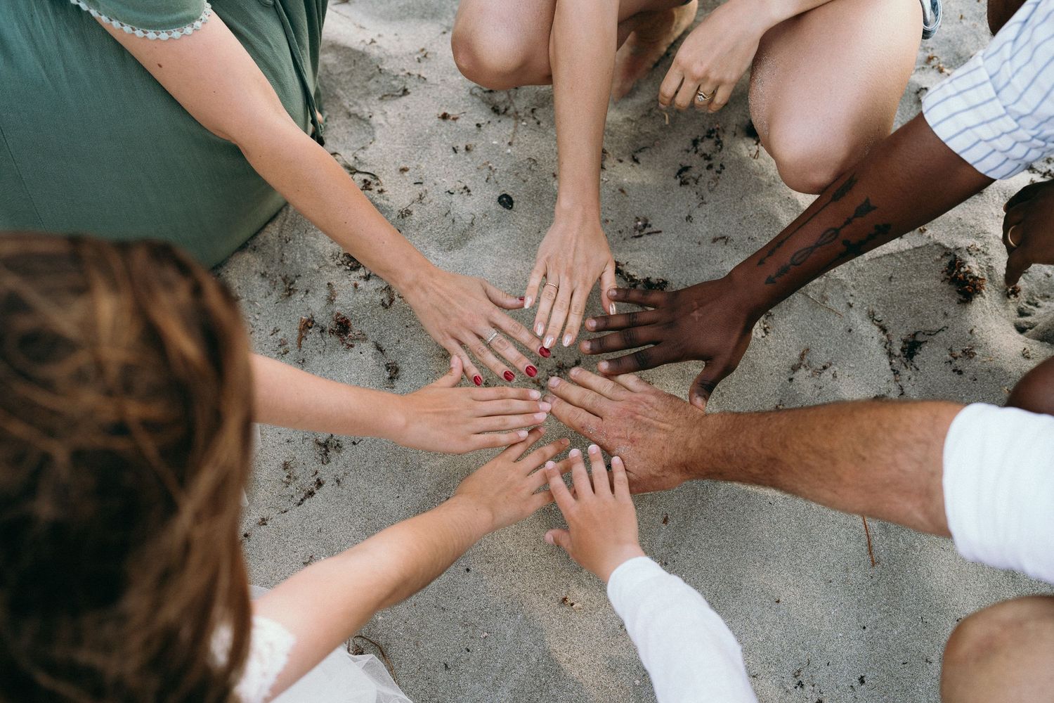 Diverse group of people joining hands together in a circle on sandy beach, symbolizing unity and teamwork.