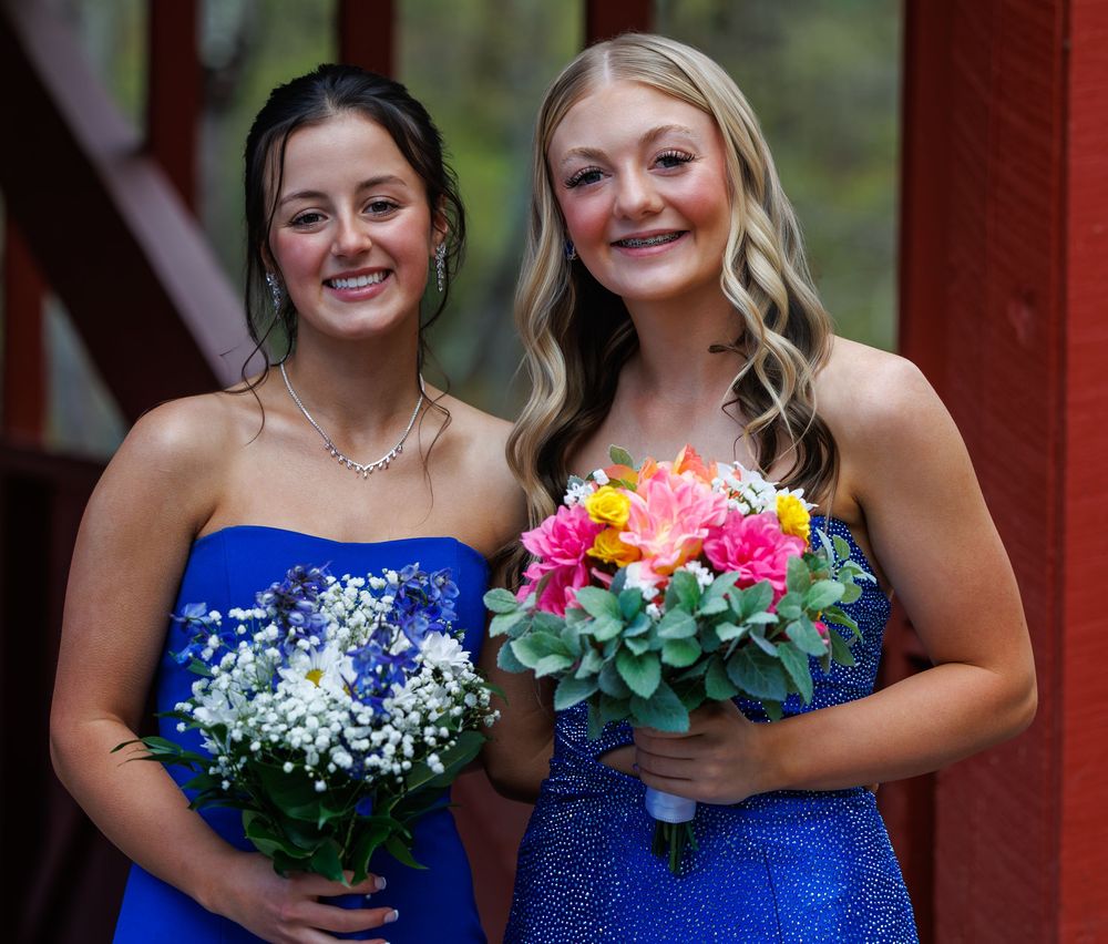 Two young women in blue strapless dresses holding bouquets of flowers, smiling at a formal event.