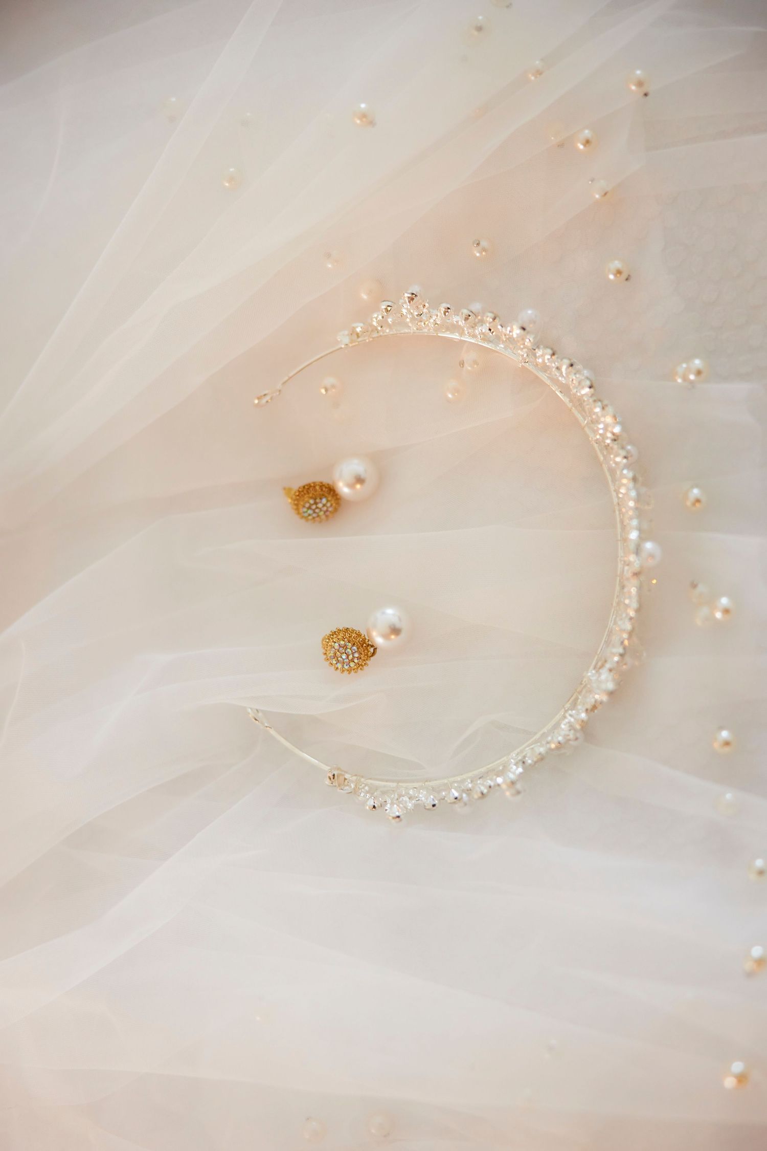 Elegant bridal tiara with crystals and pearl drop earrings on soft ivory tulle wedding veil fabric.