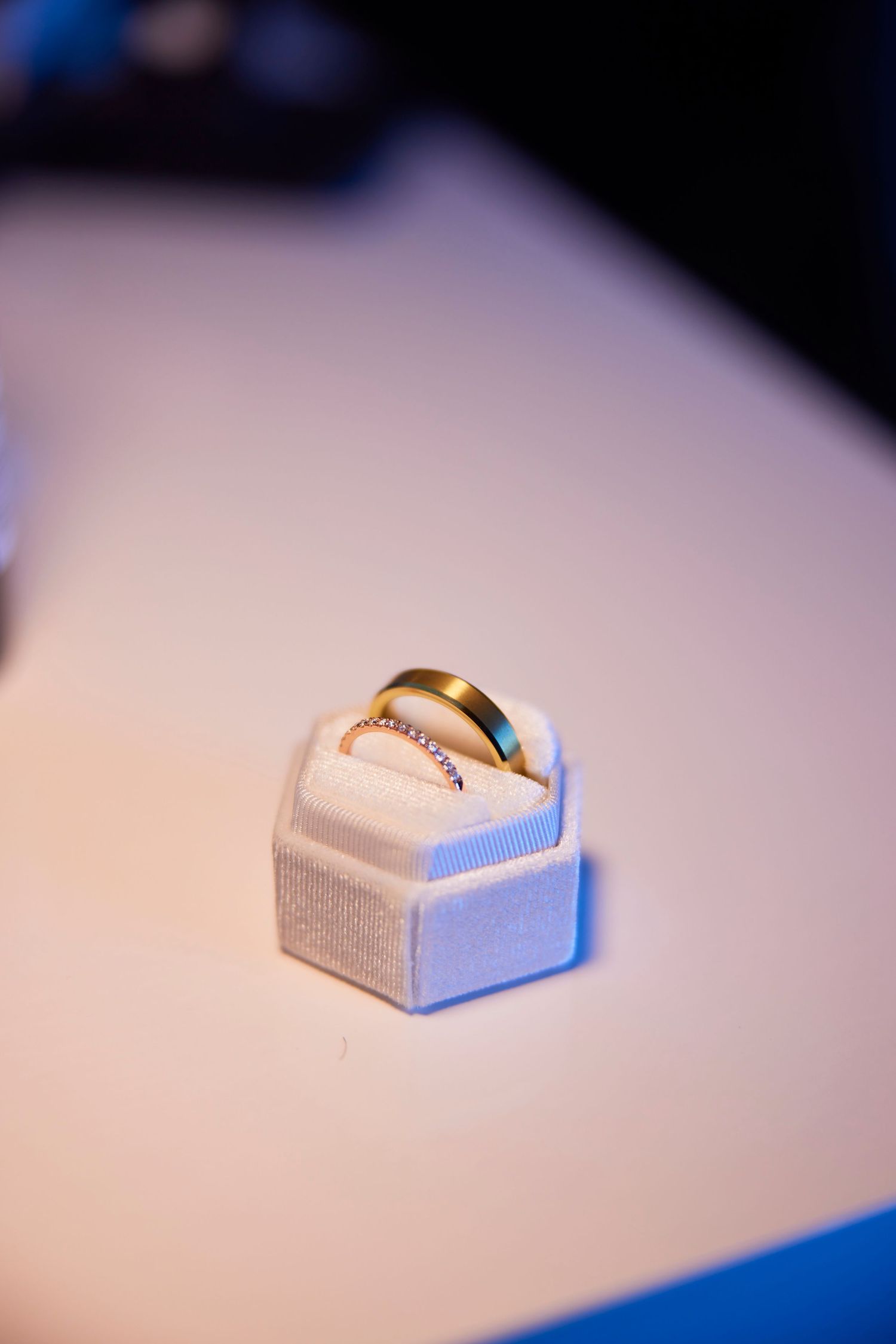 Two gold wedding rings displayed in a white velvet hexagonal ring box on a white surface.