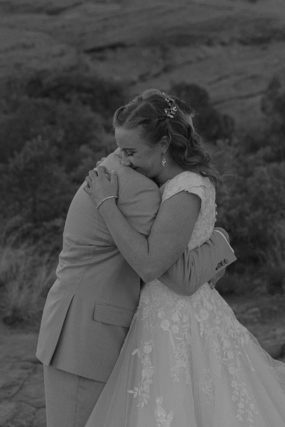 Black and white photo of a bride and groom sharing an emotional embrace on their wedding day outdoors.