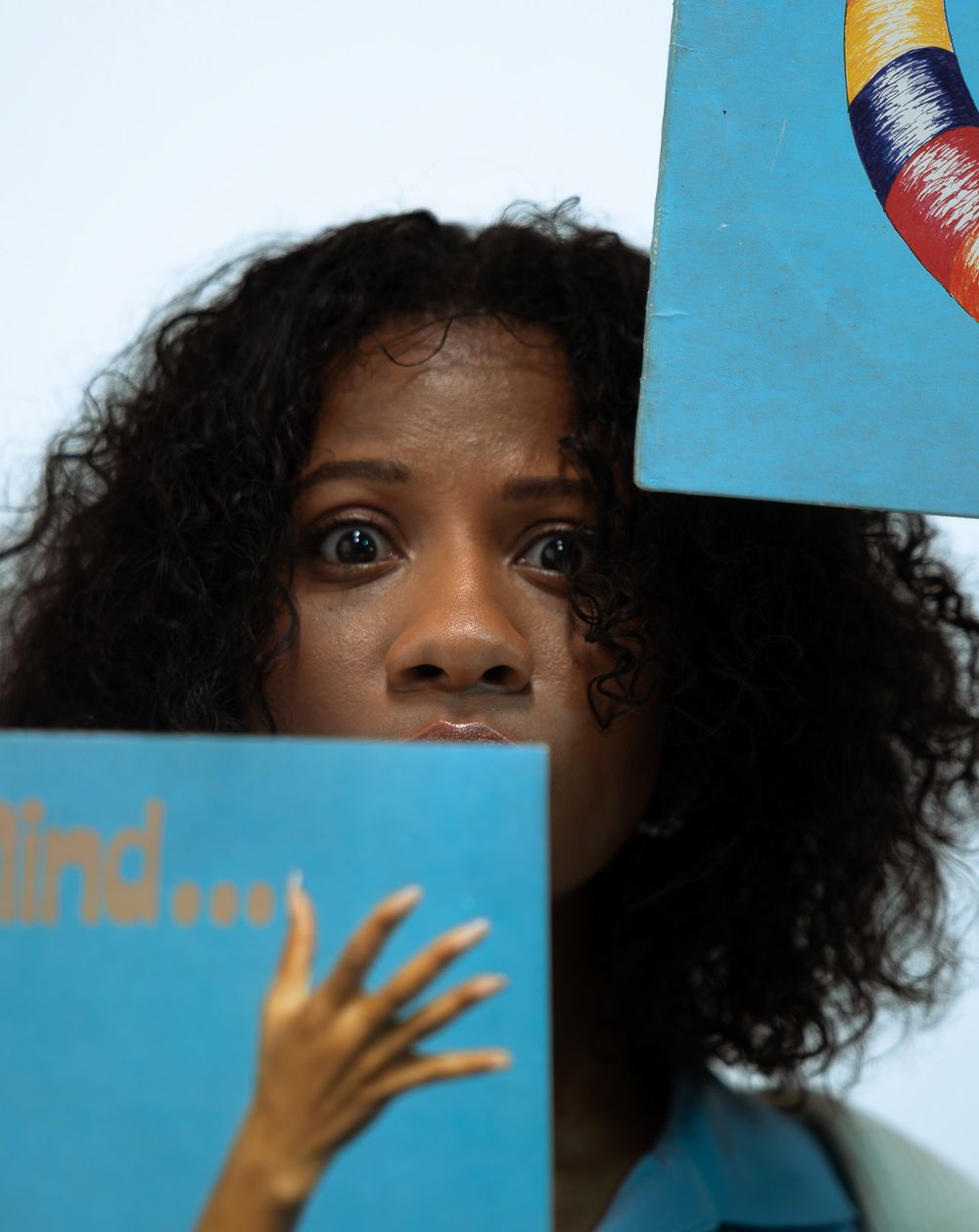 A woman with curly hair peeks over blue books, one reading 'mind...', with a colorful artwork visible above.