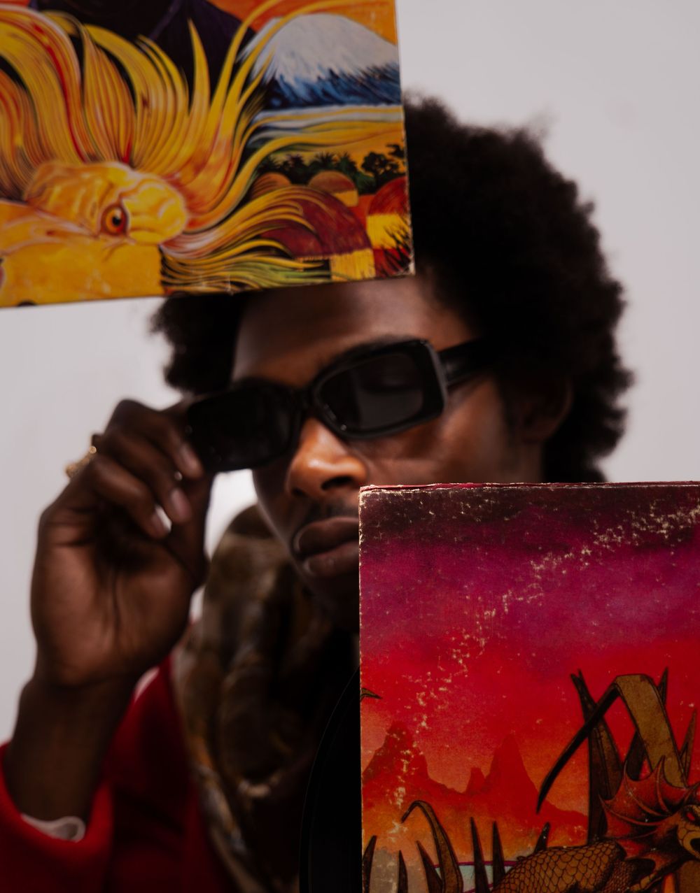 A person with an afro and sunglasses holds colorful dragon artwork panels in front of their face.
