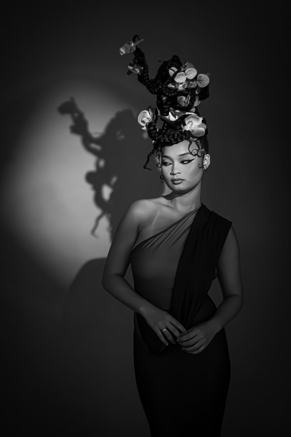 Black and white portrait of a woman in an elegant one-shoulder gown wearing an elaborate floral headpiece.