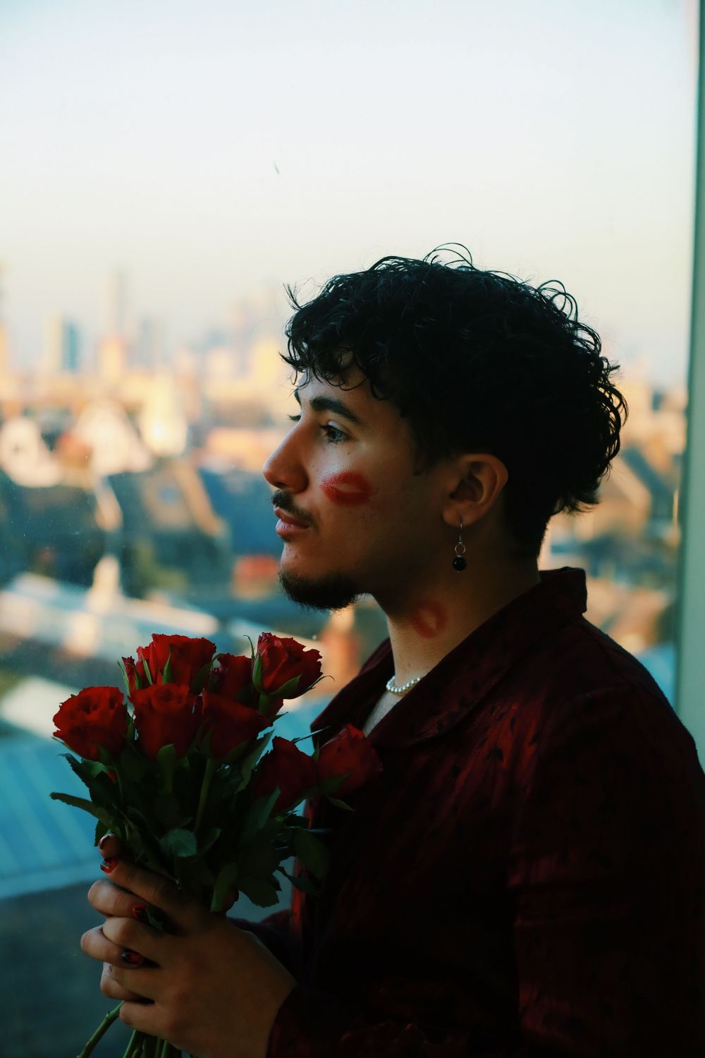Romantic portrait with red roses against a city skyline background at dusk.