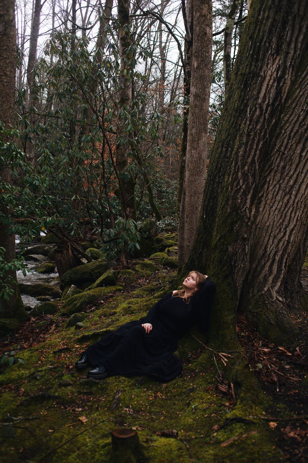 Dramatic fashion photo of someone lying on mossy ground in a dark forest wearing black clothing.