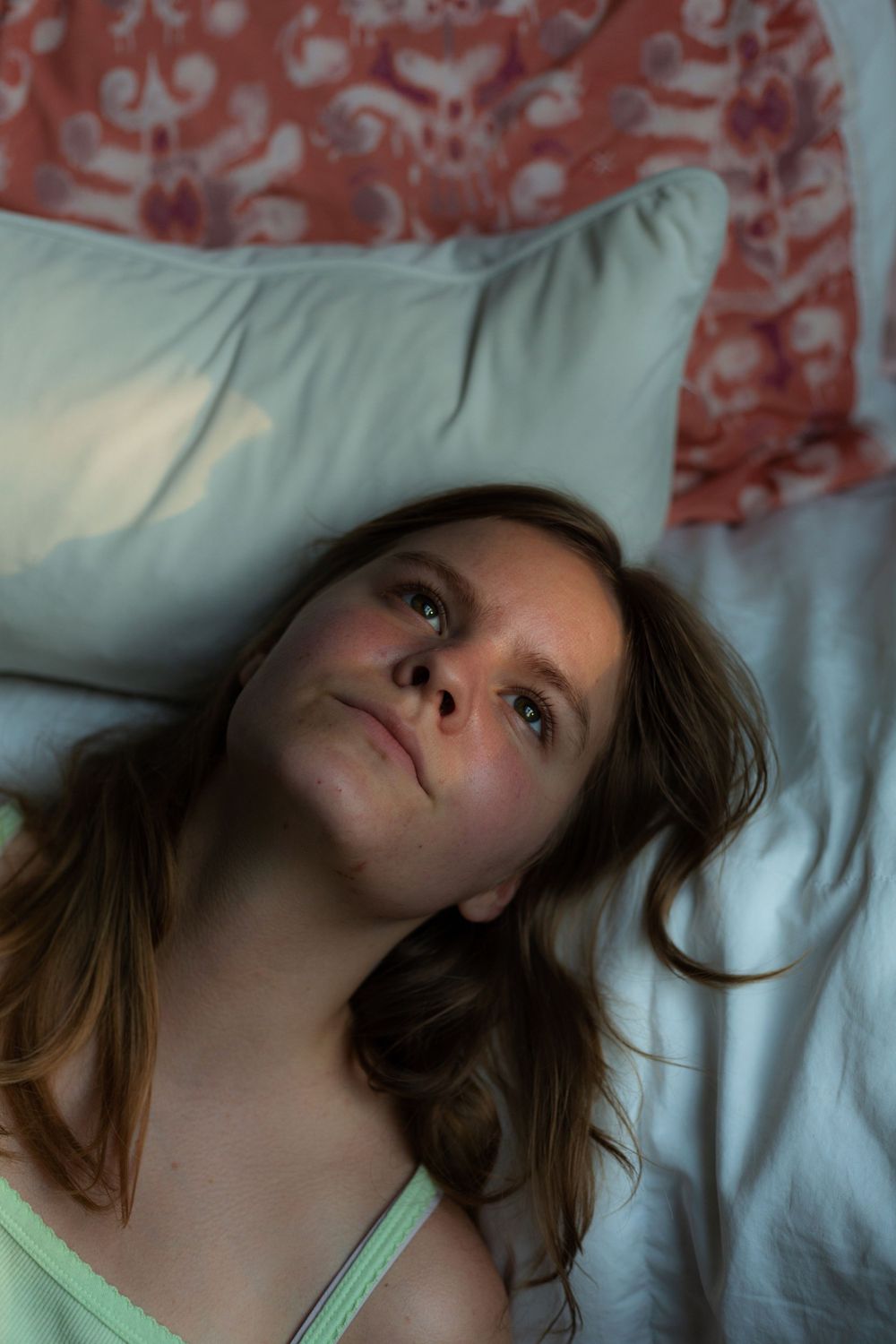 Soft intimate portrait of a person lying on a bed with red patterned decor.