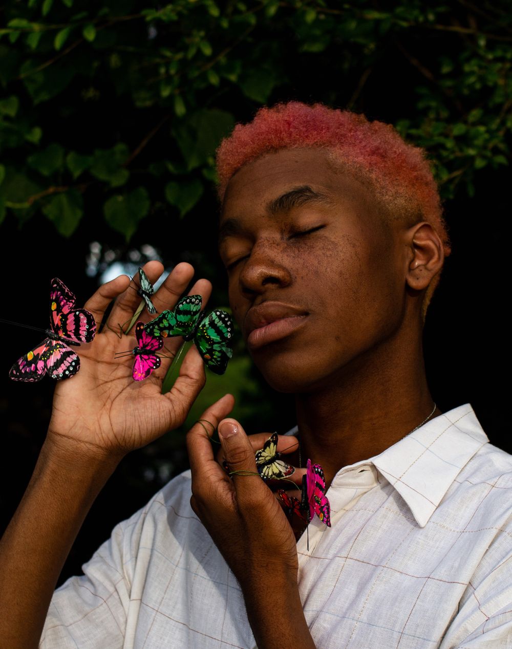 Creative portrait with butterflies against dark foliage background.