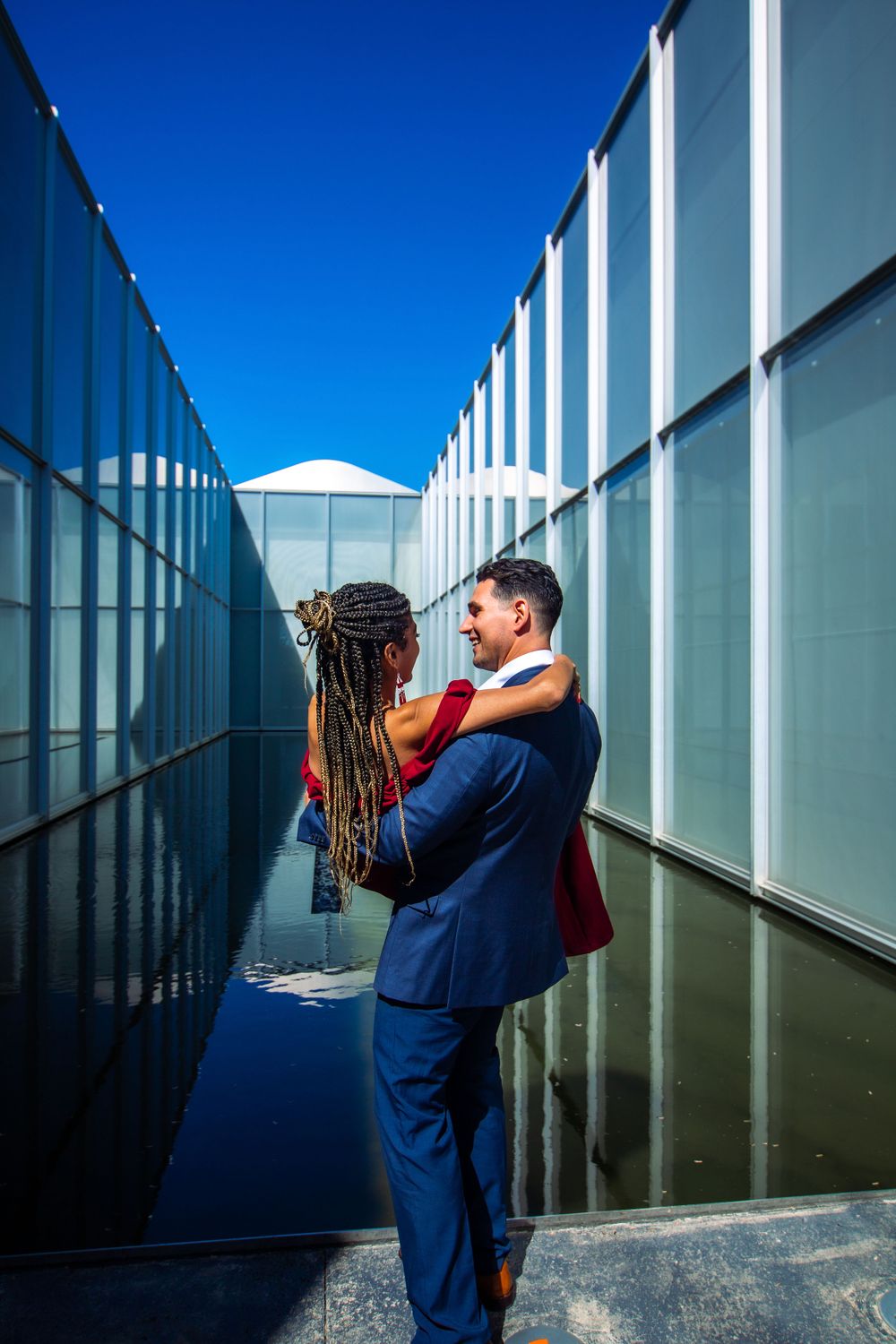 Romantic couple embracing in modern architectural corridor with blue walls and dramatic lighting.