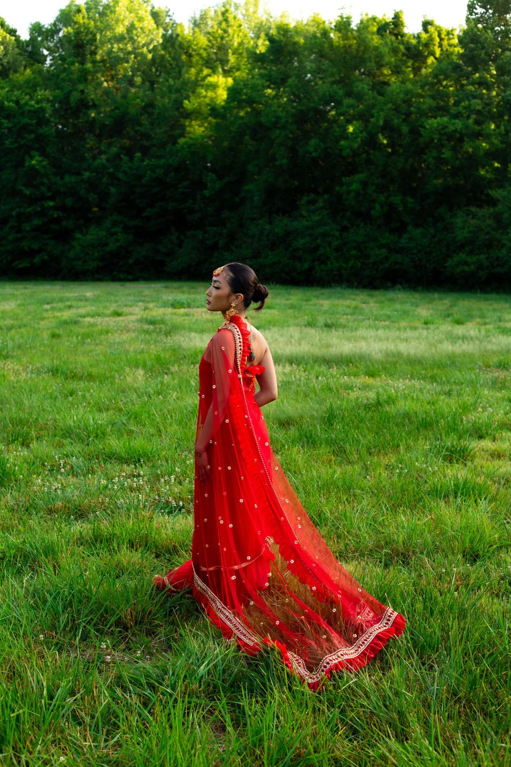 Figure in flowing red traditional dress walks through sunny green meadow.