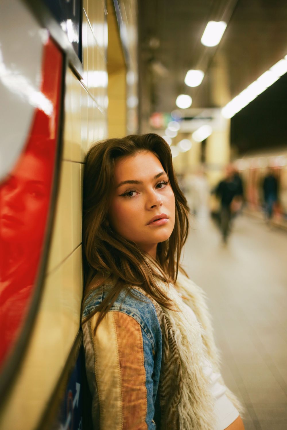 Fashion portrait taken in a subway station with someone wearing a fur vest and denim outfit.