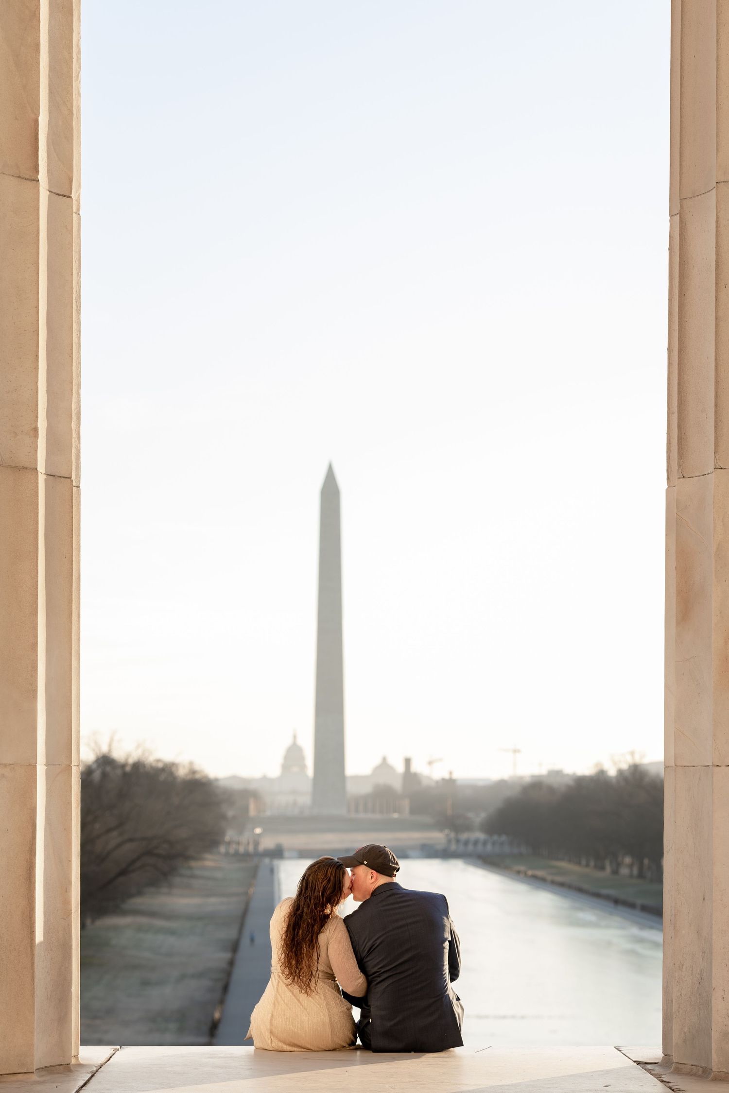 Couple sits together overlooking the Washington Monument and Reflecting Pool at at the Lincoln Memorial during sunrise.