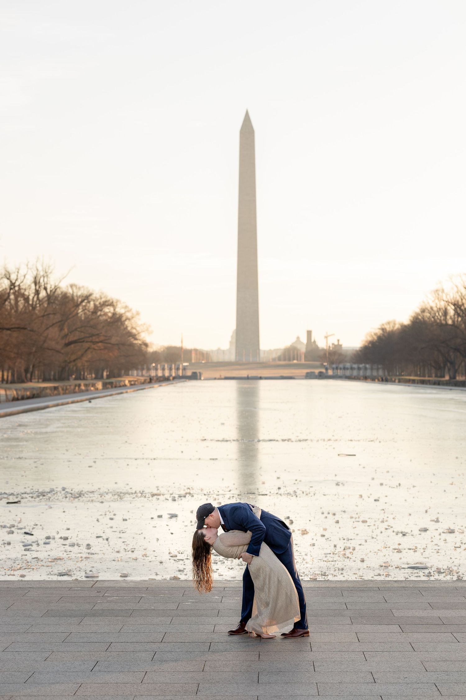Romantic dip pose with Washington Monument and reflecting pool creating dramatic backdrop.